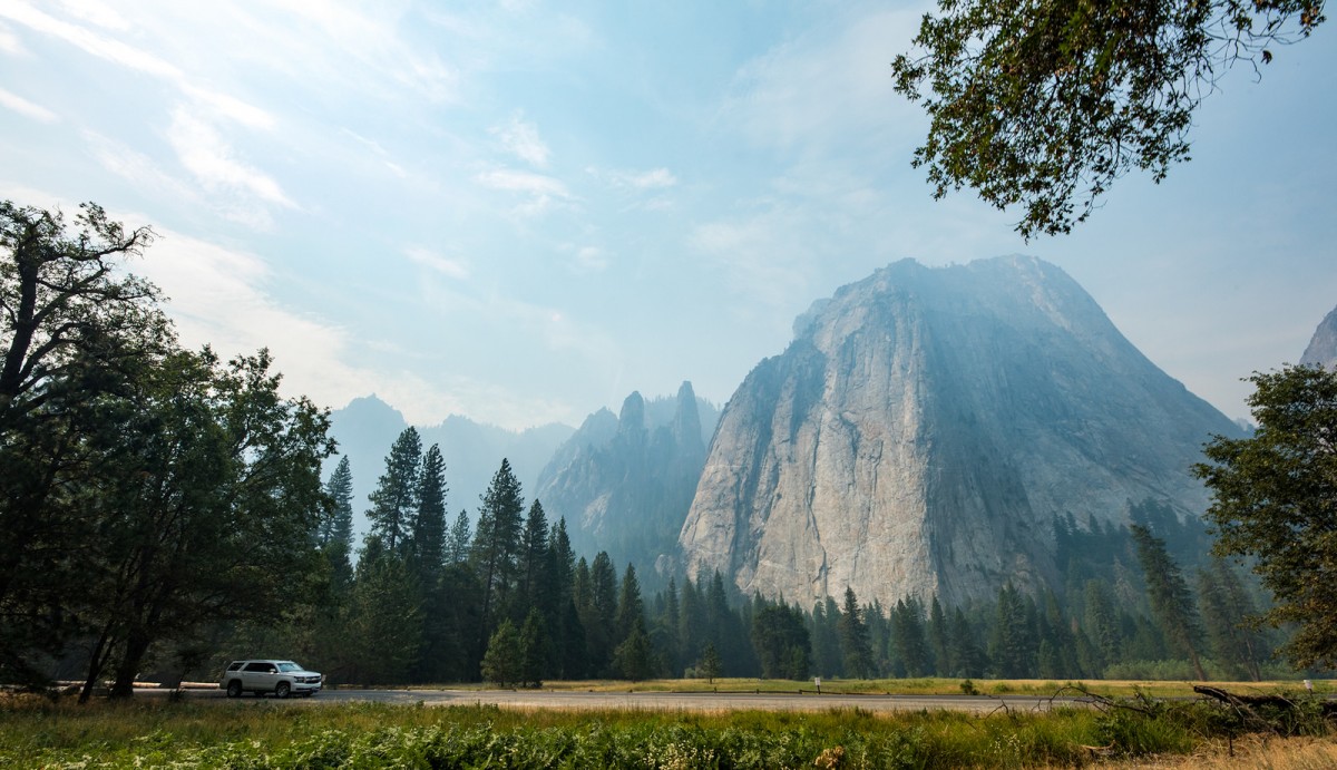 SUV drives through Yosemite as the mountaians tower in the distance.