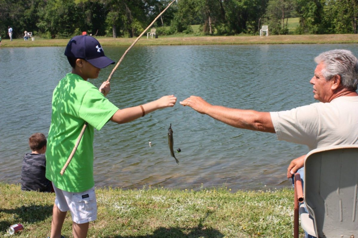 Man helping a child handle a freshly caught fish.