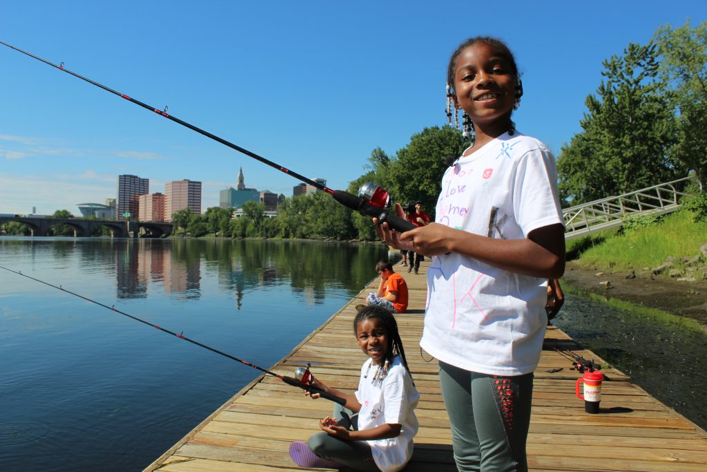 Children smiling while fishing from a wooden dock.
